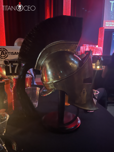 Titan 100 Event 4 | AJ Adhesives The Titan 100 Bronze Roman-style helmet with a black plume on a table at the event.